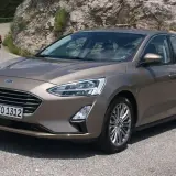 Brązowy Ford Focus MK3 1.6 TDCI na krętej drodze, z motocyklistą w tle.