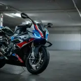 Sportowy motocykl BMW XR w biało-niebiesko-czerwonych barwach, z włączonymi światłami LED, stoi na betonowej posadzce w garażu.