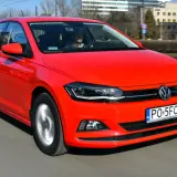 Czerwony Volkswagen Polo 6 w ruchu miejskim. Kierowca w szarej bluzie prowadzi auto.