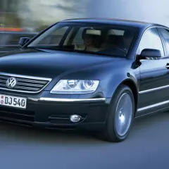 Elegancki, czarny Volkswagen Phaeton w ruchu, z parą pasażerów w środku.