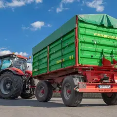 Czerwony traktor z zieloną przyczepą. Zastanawiasz się, ile można jechać z przyczepką? Ten zestaw jest gotowy do pracy.