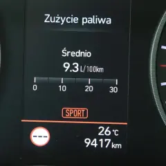 Na wyświetlaczu samochodu widać licznik spalania paliwa: średnie zużycie 9.3 L/100km. Obok widnieje tryb SPORT.