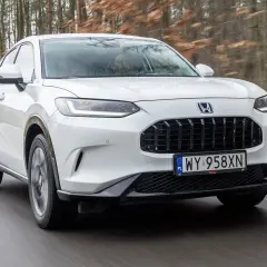 Biała Honda ZR-V przemierza leśną drogę, ukazując swój elegancki design i dynamiczną sylwetkę.
