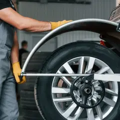 Mechanik w żółtych rękawiczkach ustawia koło na wyważarce. Dowiedz się, ile kosztuje wyważenie kół.