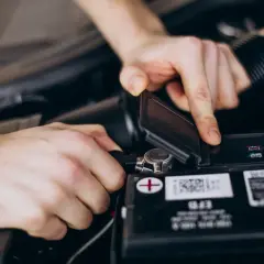 Ręce mechanika przy samochodowym akumulatorze. Widać różne rodzaje akumulatorów i ich oznaczenia.