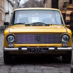 Żółty klasyk z rejestracją 19:39 LVK na brukowanej ulicy.