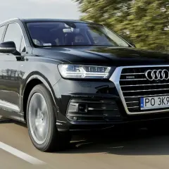 Czarny Audi Q7 3.0 TDI pędzi po drodze, otoczony zielenią drzew.