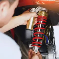 Mechanik dokonuje wymiany amortyzatorów w motocyklu, trzymając nowy element.