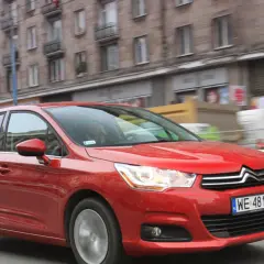 Czerwony Citroen C4 1.6 HDi w ruchu miejskim, z rozmytym tłem budynków i innych pojazdów.