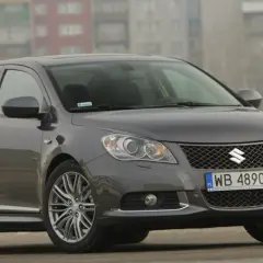 Szary Suzuki Kizashi z polskimi tablicami WB 4890E zaparkowany na tle bloków mieszkalnych.