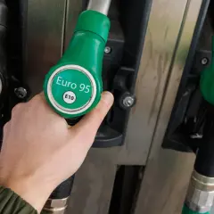 Dłoń wybiera dystrybutor z napisem "Euro 95 E10", czyli benzyna bezołowiowa. Obok widać dystrybutory Diesel i Super+ 98.