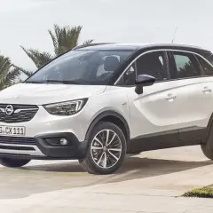 Biały Opel Crossland z czarnym dachem, zaparkowany na tarasie przy basenie. Wiele osób szuka opinii o tym modelu.