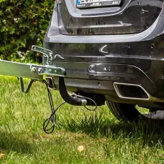 Montaż haka holowniczego w czarnym Volvo. Przyczepa gotowa do drogi, zielona trawa i krzewy w tle.