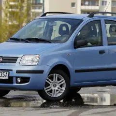 Niebieski Fiat Panda z kierowcą, stojący na mokrej nawierzchni. Kierowca zastanawia się nad aktualną ceną gazu.