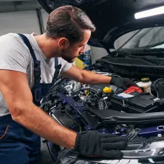 Mechanik w warsztacie dokonuje odsiarczania akumulatora w samochodzie, pracując przy otwartej masce.