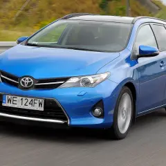 Niebieski Toyota Auris 1.6 benzyna w wersji kombi jedzie po drodze.