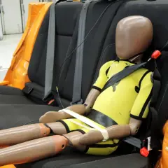 Manekin dziecka w żółtym kombinezonie, zapięty pasami bezpieczeństwa w samochodzie. To dowód, że nawet smart kid belt mandat nie chroni przed wypadkiem.