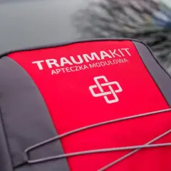 Czerwono-szara apteczka "Trauma Kit" z symbolem krzyża. Czy apteczka jest obowiązkowa w samochodzie? Zawsze warto ją mieć!