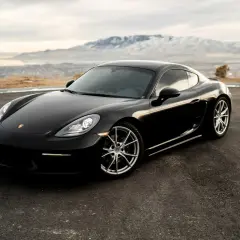 Czarne Porsche Cayman na tle gór i jeziora. Zastanawiasz się, ile kosztuje Porsche?