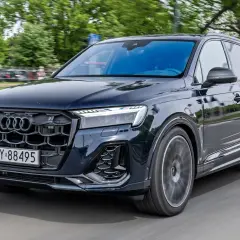 Ciemny Audi Q7 w ruchu ulicznym. Zbliżenie na przednią część pojazdu, widoczna atrapa chłodnicy i reflektory. Poznaj audi q7 wymiary.