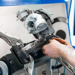 Mechanik naprawia turbosprężarkę, mocując ją imadłem. Widoczny jest zawór N75, kluczowy element sterujący pracą turbiny.