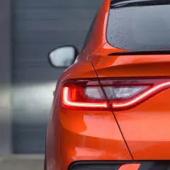 Pomarańczowy Renault Arkana z włączonymi światłami LED. Zbliżenie na tylną część auta, gdzie widoczne są detale nadwozia i nazwa modelu. Idealne wymiary dla miejskiej dżungli.