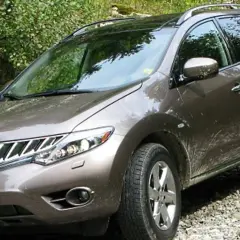 Brązowy Nissan Murano na kamienistej drodze, otoczony zielenią.