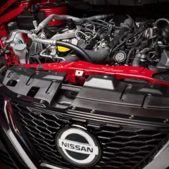 Silnik 1.6 benzyna w Nissan Qashqai. Czerwone elementy karoserii i skomplikowana sieć przewodów pod maską.