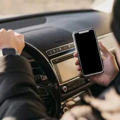 Kierowca trzyma telefon podczas jazdy, ryzykując mandat za telefon.
