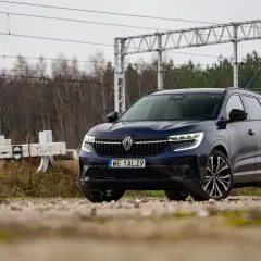 Nowy Renault Espace 2024, ciemnoniebieski SUV, zaparkowany przy torach kolejowych, gotowy na przygodę.