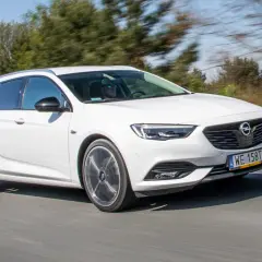 Białe kombi Opel Insignia 2.0 CDTI pędzi po drodze, za kierownicą mężczyzna w okularach przeciwsłonecznych.