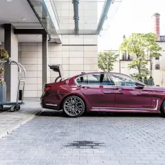 Eleganckie bmw g11 w kolorze śliwkowym z otwartym bagażnikiem stoi przed hotelem obok wózka na bagaż.