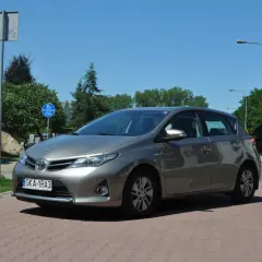 Szary Toyota Auris na tle zieleni i błękitnego nieba. Wiele osób szuka toyota auris opinie przed zakupem.