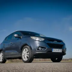 Szary Hyundai ix35 na tle błękitnego nieba. W tle komin z dymem. Wiele pozytywnych hyundai ix35 opinie potwierdza jego wszechstronność.