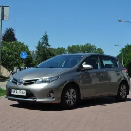 Szary Toyota Auris na tle zieleni i błękitnego nieba. Wiele osób szuka toyota auris opinie przed zakupem.