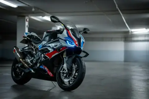 Sportowy motocykl BMW XR w biało-niebiesko-czerwonych barwach, z włączonymi światłami LED, stoi na betonowej posadzce w garażu.