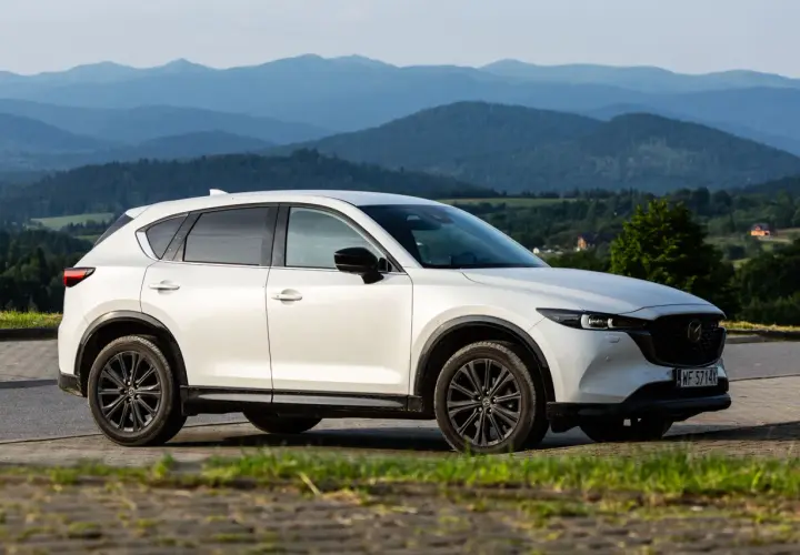 Biała Mazda CX-5 z czarnymi felgami na tle górskiego krajobrazu. KSU rejestracja widoczna na tablicy.
