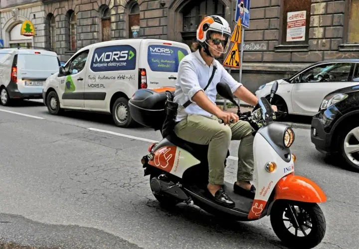 Mężczyzna w kasku jedzie skuterem elektrycznym, posiadając prawo jazdy AM. W tle białe vany dostawcze.