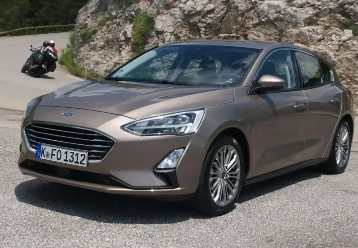 Brązowy Ford Focus MK3 1.6 TDCI na krętej drodze, z motocyklistą w tle.