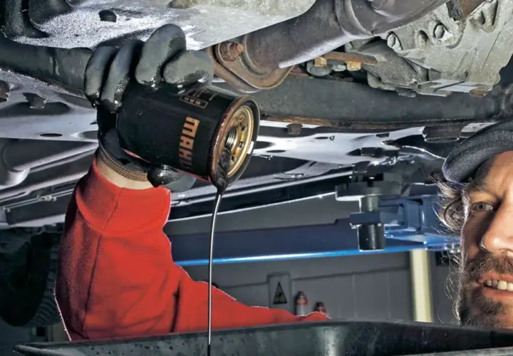 Mechanik w czerwonej bluzie wymienia stary olej z silnika. Pamiętaj, co ile wymiana oleju, by auto służyło latami.