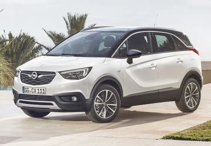 Biały Opel Crossland z czarnym dachem, zaparkowany na tarasie przy basenie. Wiele osób szuka opinii o tym modelu.