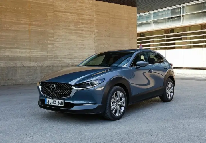 Szary Mazda CX-30 stoi przed betonową ścianą. Wady tego modelu to m.in. ograniczona widoczność z tyłu.
