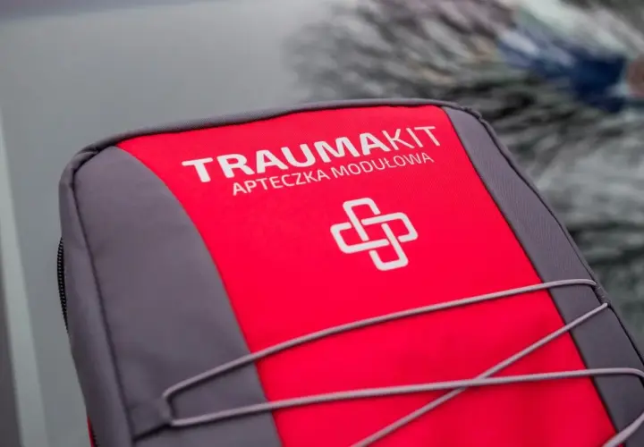 Czerwono-szara apteczka "Trauma Kit" z symbolem krzyża. Czy apteczka jest obowiązkowa w samochodzie? Zawsze warto ją mieć!