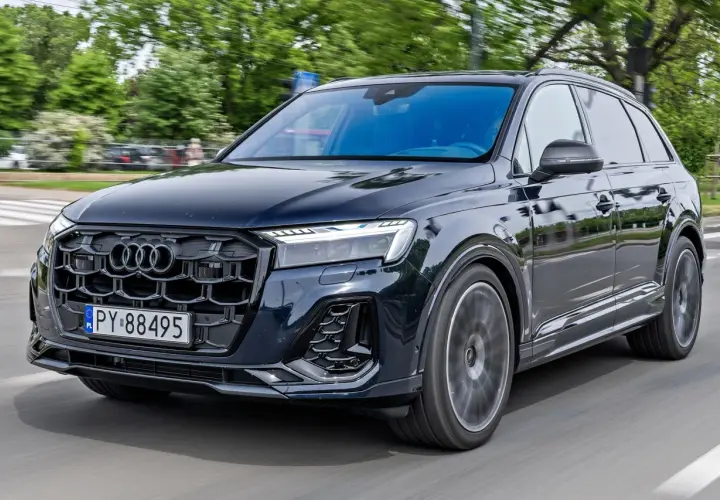 Ciemny Audi Q7 w ruchu ulicznym. Zbliżenie na przednią część pojazdu, widoczna atrapa chłodnicy i reflektory. Poznaj audi q7 wymiary.