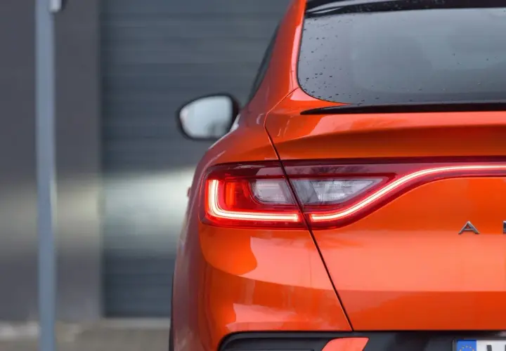 Pomarańczowy Renault Arkana z włączonymi światłami LED. Zbliżenie na tylną część auta, gdzie widoczne są detale nadwozia i nazwa modelu. Idealne wymiary dla miejskiej dżungli.