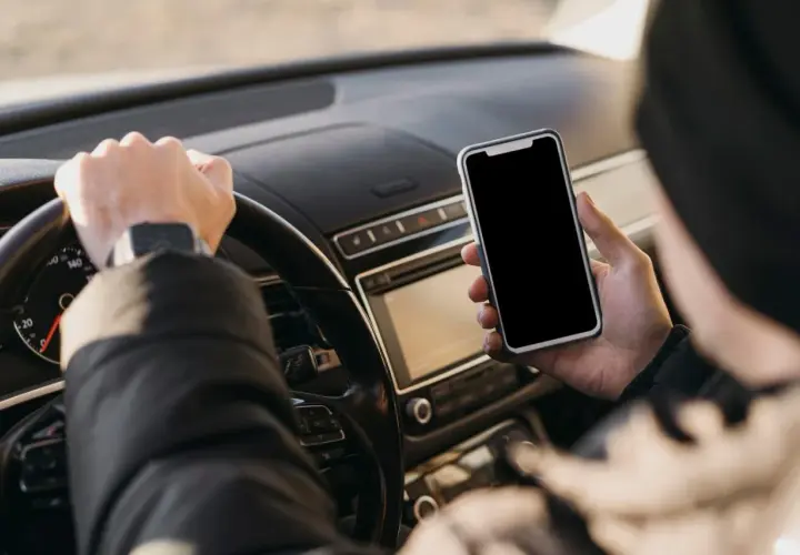 Kierowca trzyma telefon podczas jazdy, ryzykując mandat za telefon.