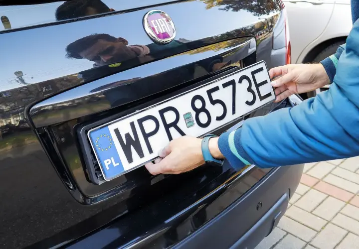 Ręce montują tablicę rejestracyjną WPR 8573E na czarnym samochodzie. To duplikat tablicy rejestracyjnej.