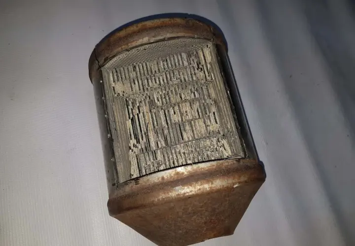 Zardzewiały, uszkodzony katalizator samochodowy, przypominający strukturą plaster miodu. FAP w złym stanie.