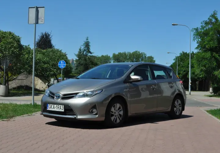 Szary Toyota Auris na tle zieleni i błękitnego nieba. Wiele osób szuka toyota auris opinie przed zakupem.