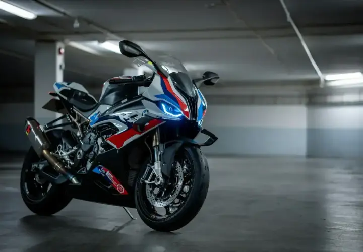 Sportowy motocykl BMW XR w biało-niebiesko-czerwonych barwach, z włączonymi światłami LED, stoi na betonowej posadzce w garażu.